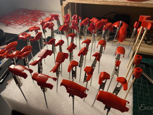 A picture of red gundam parts on sticks stuck into a foam block.