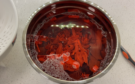 A picture of red gundam parts in a steel bowl filled with soapy water.