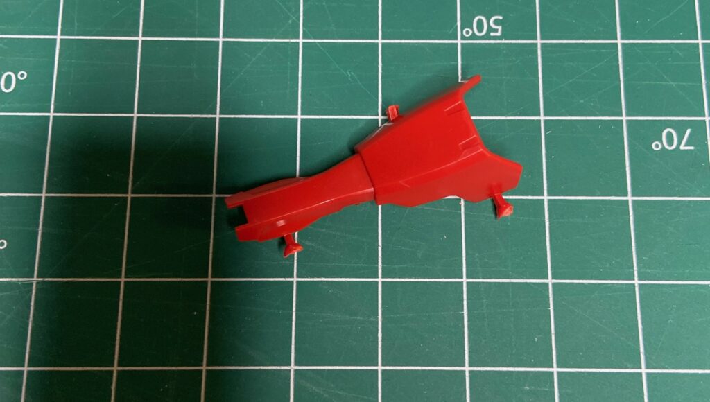 A red gunpla part that has been cut out and has excess plastic nubs from where it was cut off of the runner.