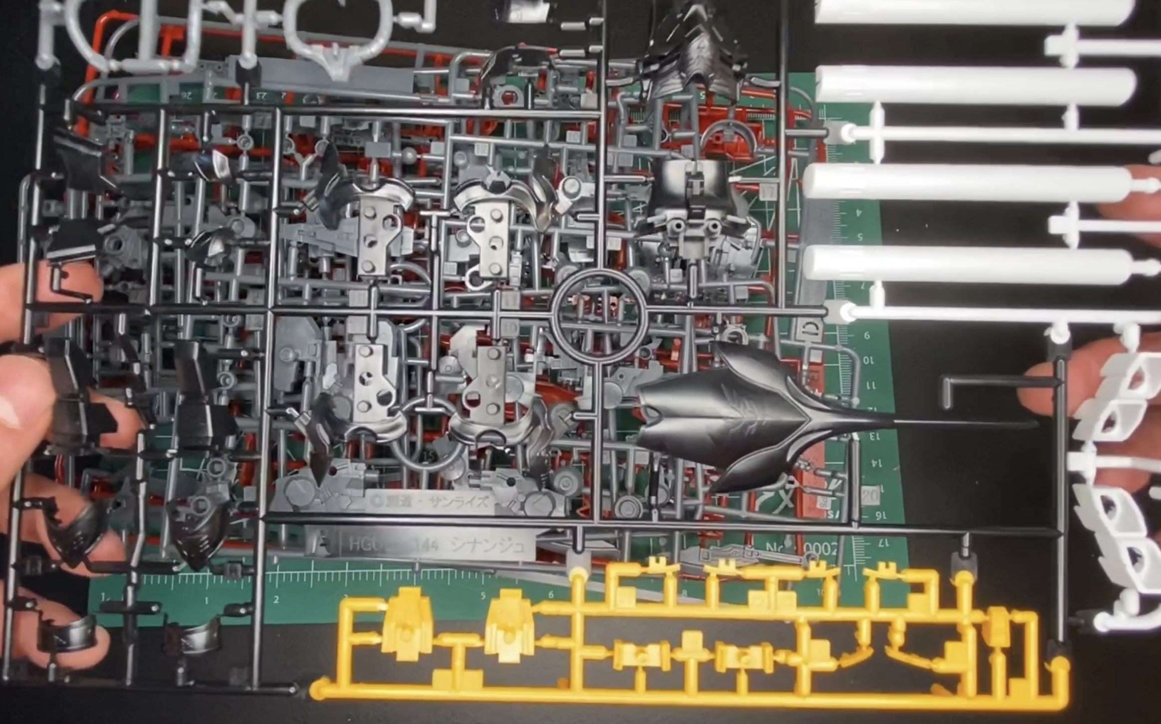 A picture of a plastic grid of black, white and yellow gunpla parts.