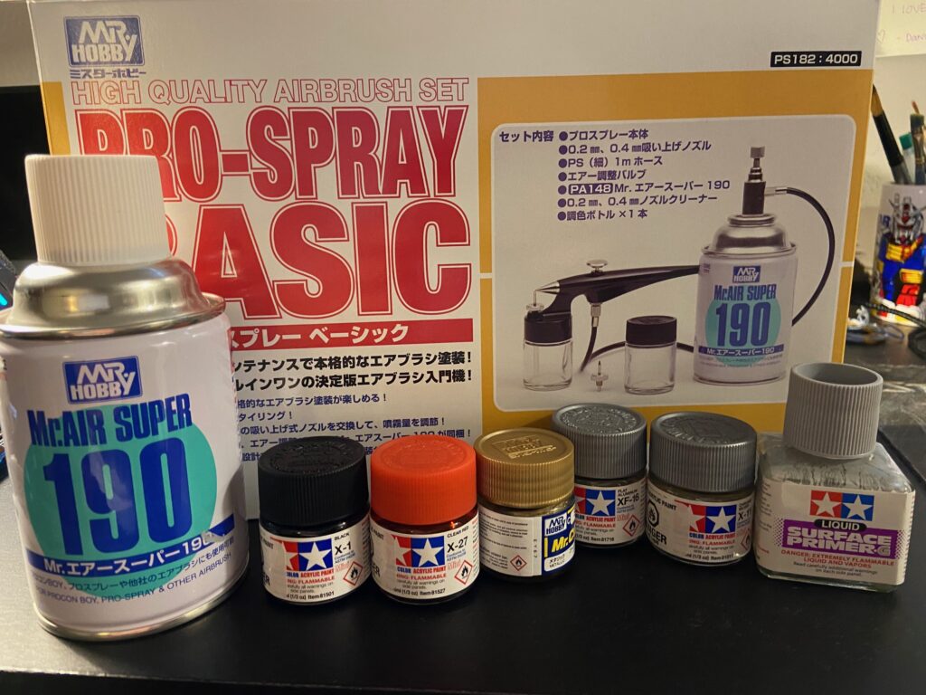 Image of an airbrush box accompanied by a compressed air can and various coloured bottles of paint.